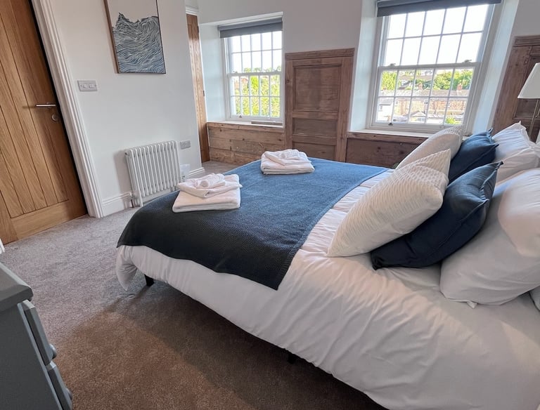Finished bedroom with soft furnishings, wooden floors, and large sash windows.