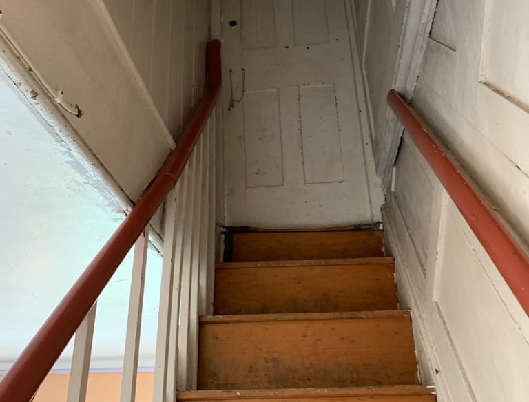 Narrow wooden staircase with painted banisters before refurbishment.