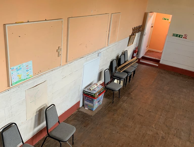 Empty classroom with noticeboards, stacked chairs, and exposed walls during early works.