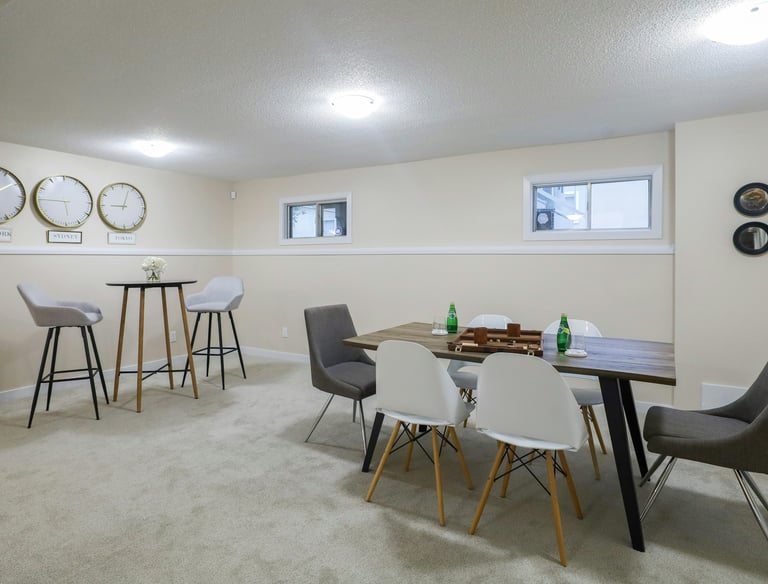 Modern finished basement featuring a wooden dining table with Eames-style chairs and a high-top bistro set.