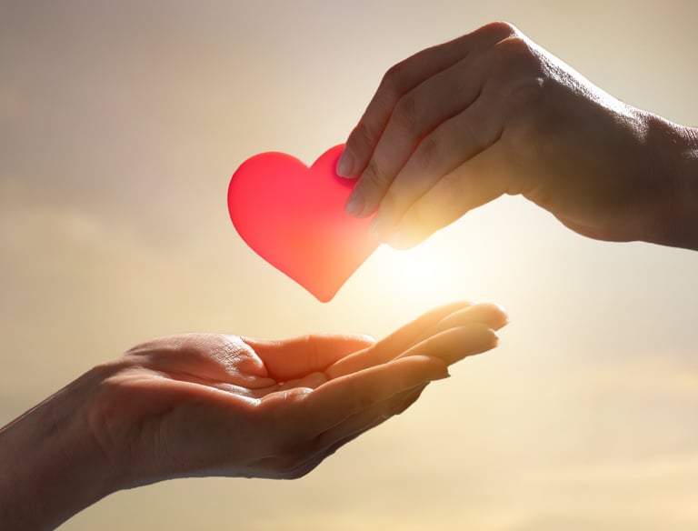 Hand placing a red heart into another person’s open hands