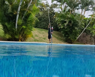 Técnico profissional de piscinas usando uma vara telescópica para limpar uma piscina de quintal cerc
