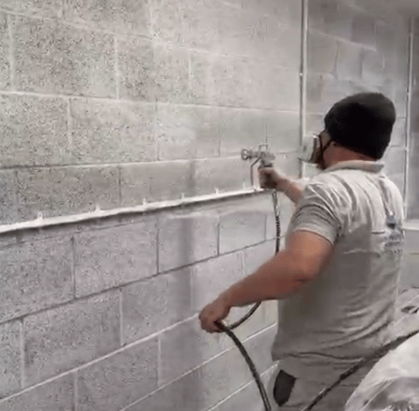 LPAD staff using a paint sprayer on an industrial cinderblock wall.