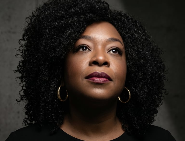 Professional portrait of a black woman with curly hair and gold hoop earrings looking upwards.