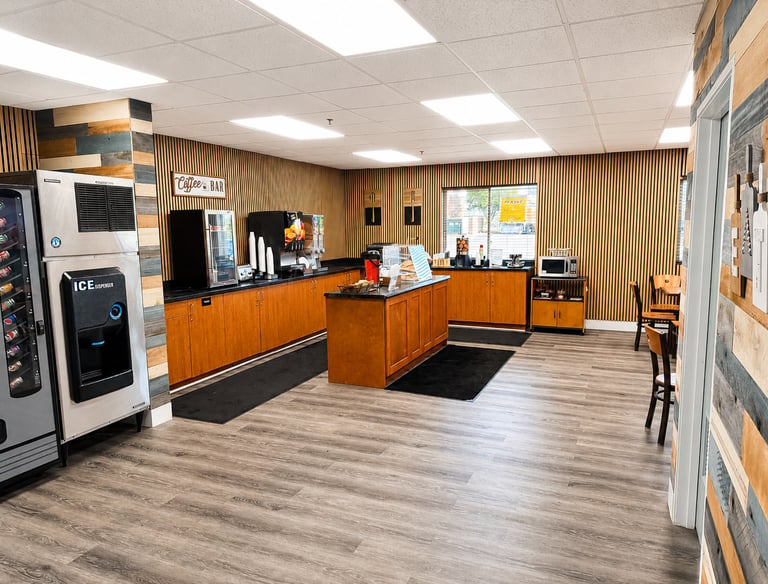 Modern hotel breakfast area and coffee bar with wood paneling, ice machine, and snack station.