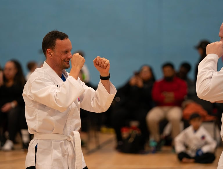 Two smiling men in white martial arts uniforms practicing karate sparring at a tournament.