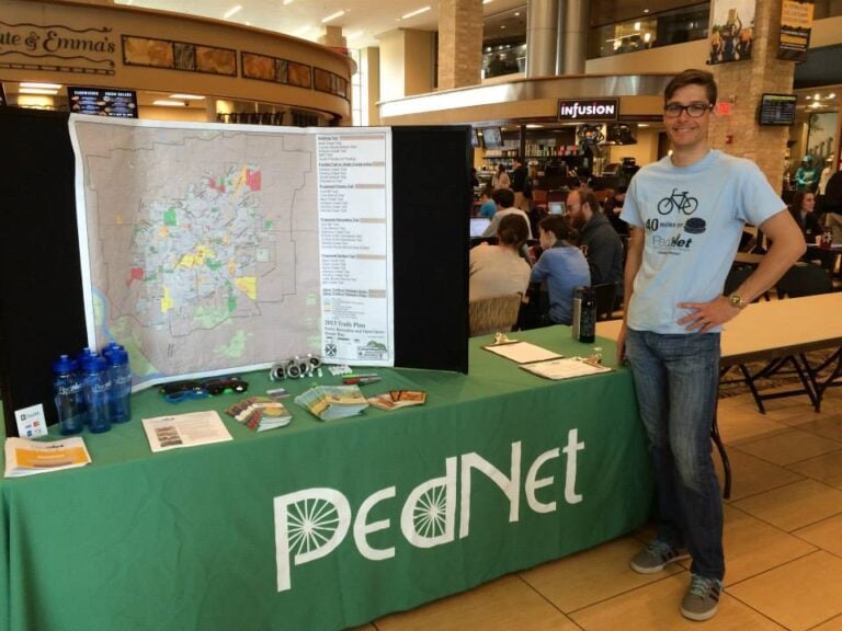 Lawrence posing by a table reading "PedNet" with a map trifold