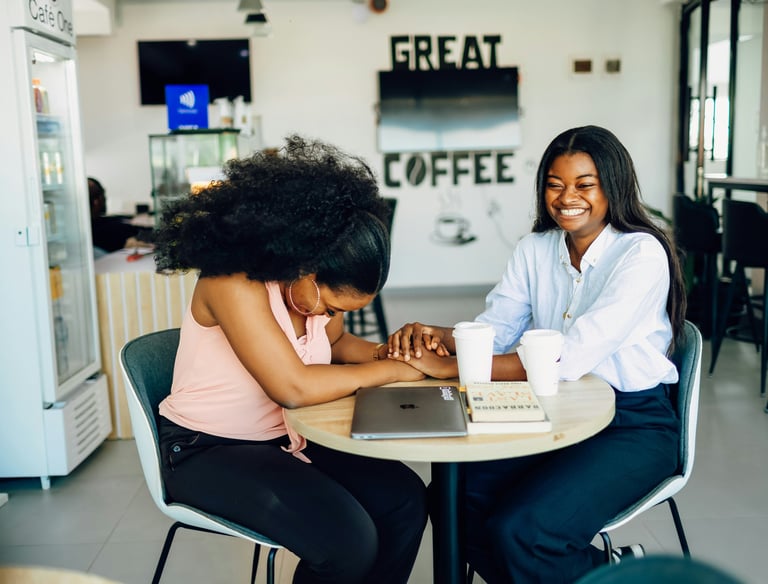 Two women sit at a table holding hands while laughing.