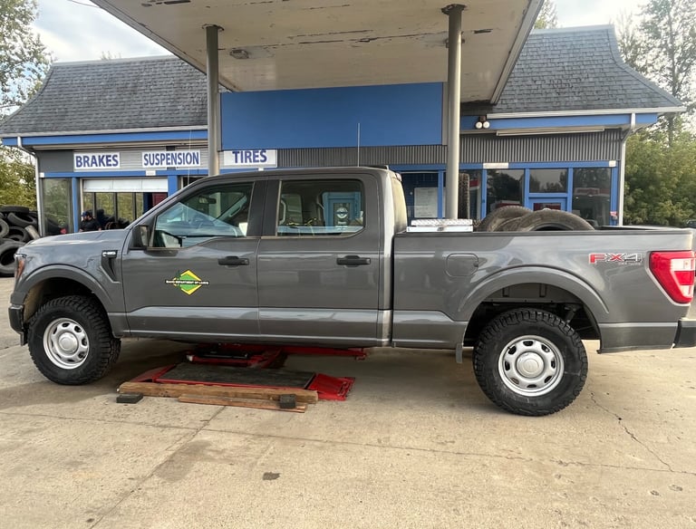 Gray Ford F-150 truck lifted on a hydraulic jack for tire service at an automotive repair shop.