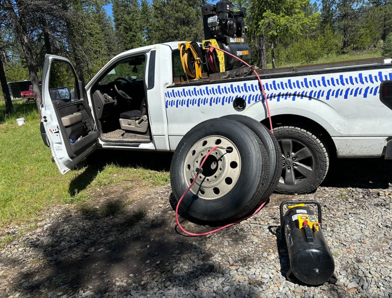 Mobile tire service truck inflating semi-truck tires with a portable air compressor in a rural area.