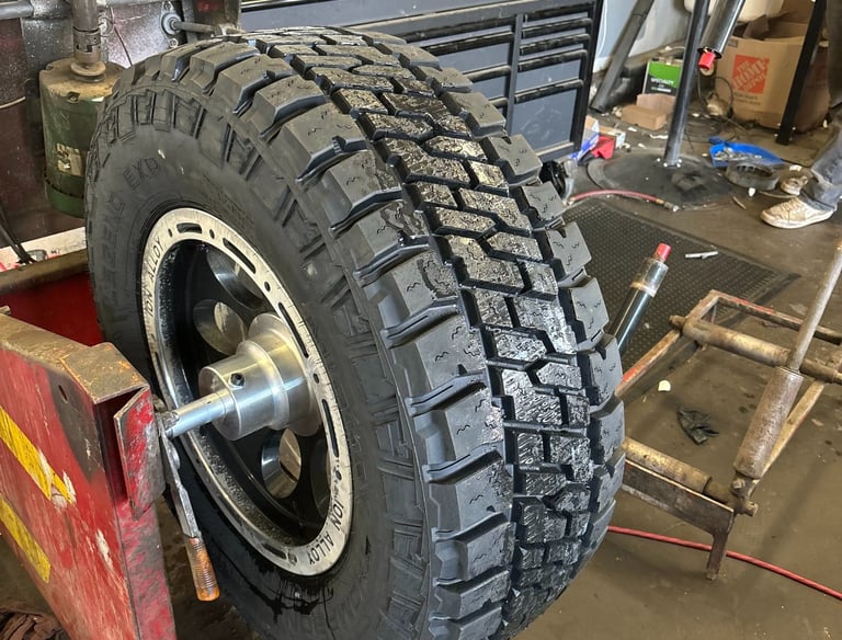 All-terrain truck tire mounted on a rim balancer in a professional automotive repair shop.