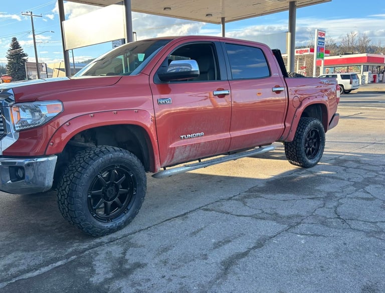 A lifted red Toyota Tundra 4x4 pickup truck with black off-road wheels parked at a gas station.
