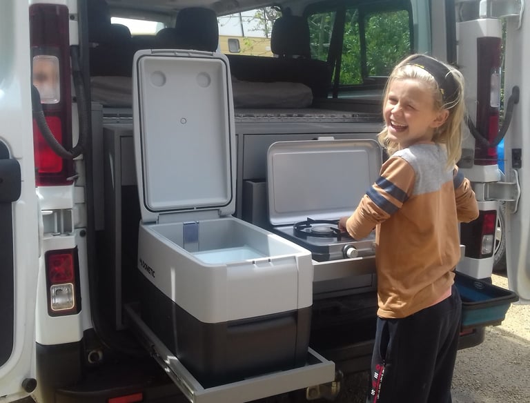 a young girl standing in front of a van with a coolerbox