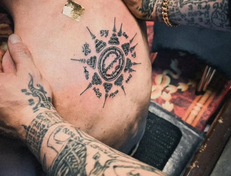a man with traditional thai sak yant tattoos on his back holded by another man with sak yant tattoos