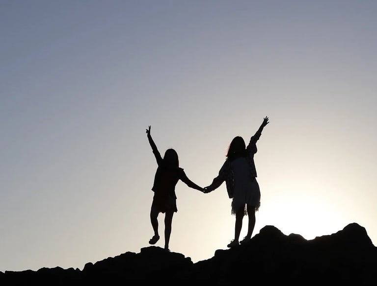 2 silhouettes de femmes qui se tiennent la main sur le haut d'une colline et qui regarde l'horizon