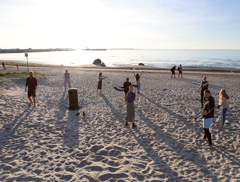 Group of people practicing flow arts and drumming together on a sandy beach in Estonia. Photo by Martin Vähk