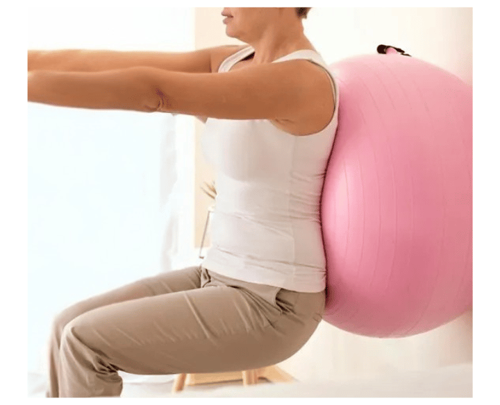 Paciente encostada na parede com uma bola rosa de pilates nas costas realizando exercício
