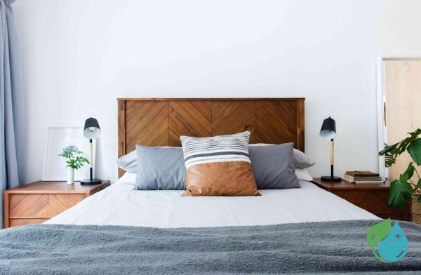 lit avec 3 oreillers, 1 drap blanc et un plaid gris foncé, avec deux commodes en bois vernis et la tête de lit également