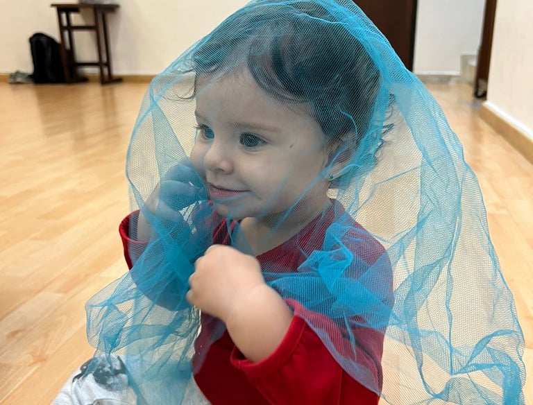 Niña sentada en piso de madera cubierta por una malla azul transparente en Ukelele Jardín Infantil