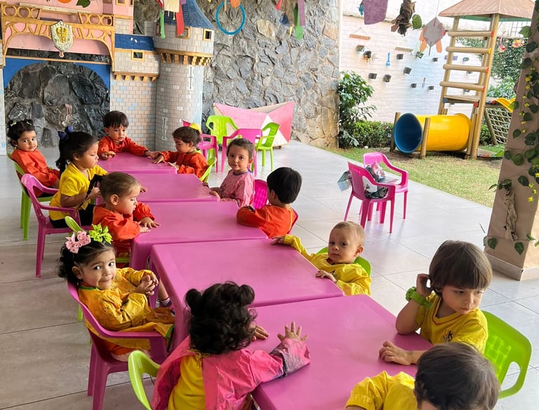 Niños sentados en mesas rosadas con sillas verdes en Jardín Infantil Ukelele