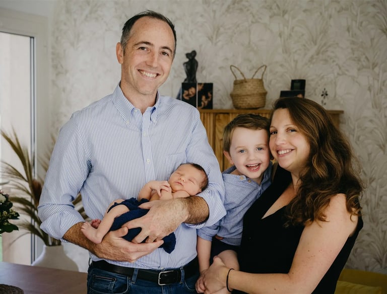 Photo de famille à domicile avec maman, papa, bébé et grand frère souriants – séance naissance Gard