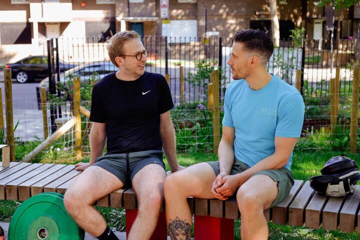 A personal trainer in a blue t-shirt sat outside talking to his client