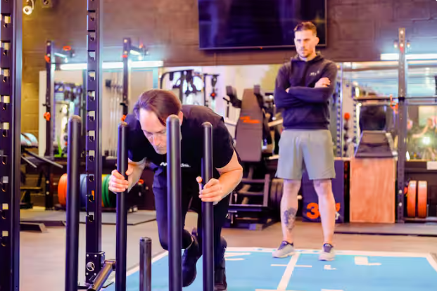 a man is pushing a prowler on a blue mat during a gym session