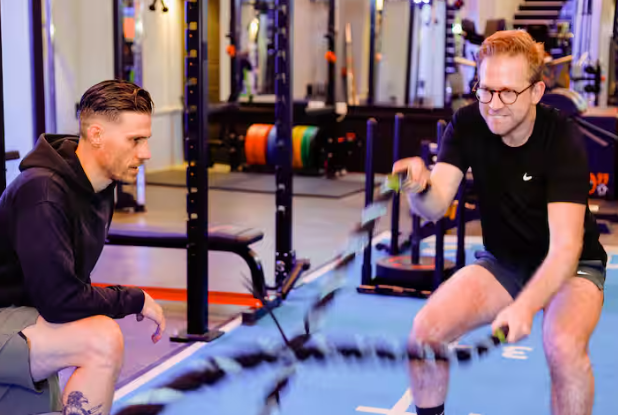 A man is exercising with battle ropes with a personal trainer