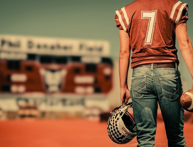 a high school graduate in a football uniform holding a football helmet
