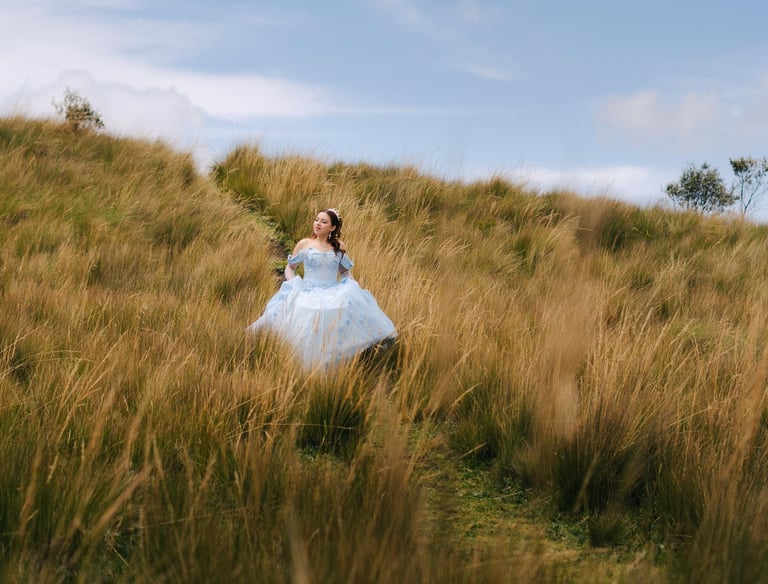 Quinceañera con vestido celeste en un pradp con paja y un cielo azul en Quito Ecuador