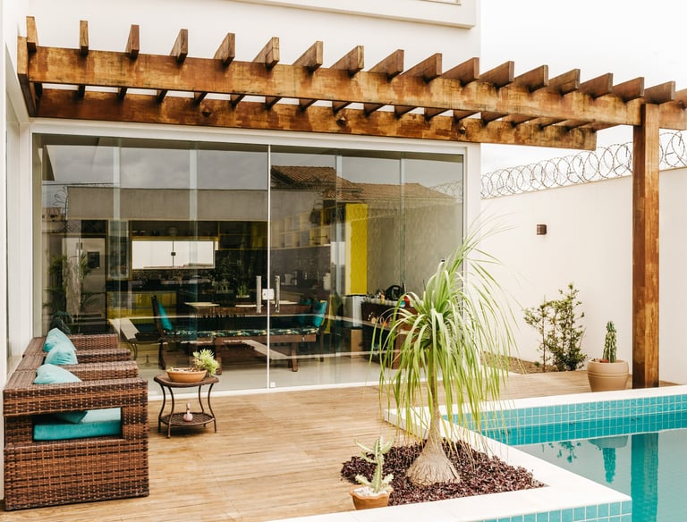 Modern backyard patio with a wooden pergola, swimming pool, and wicker lounge chairs.