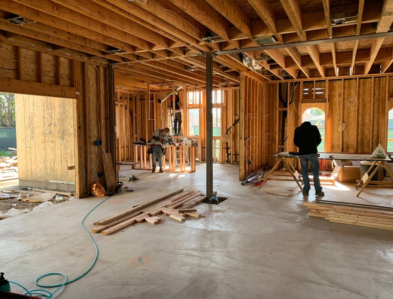Construction workers framing a new house interior with wooden studs and floor joists on a concrete slab.