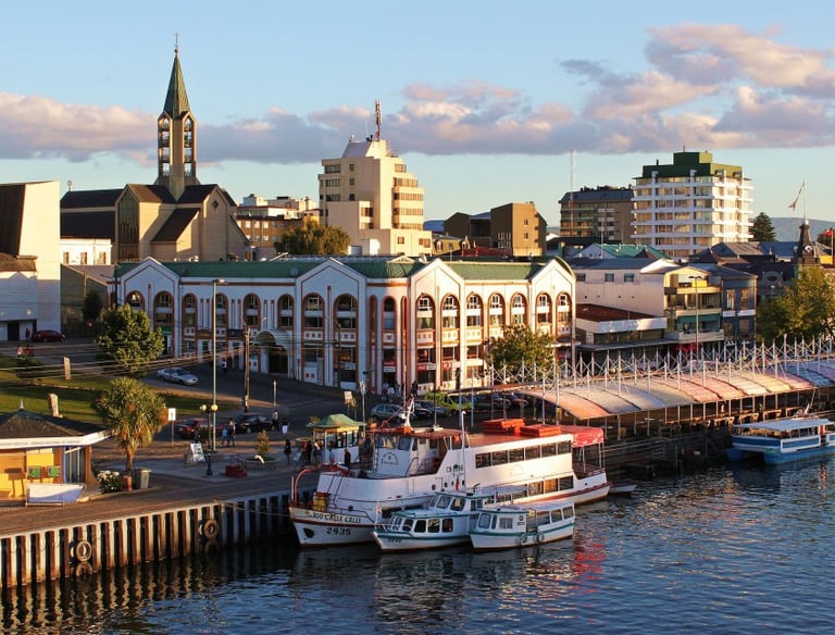 Valdivia city waterfront with tour boats docked at the pier near historic buildings and a church spire.