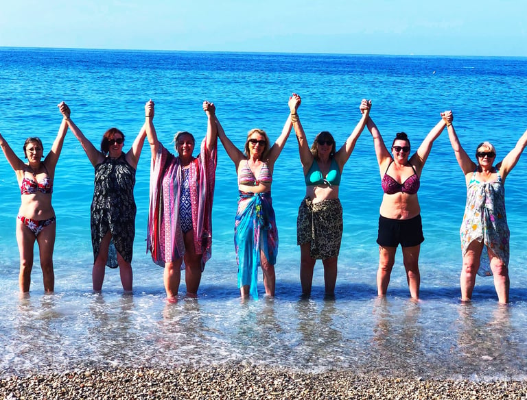 A grour of women in swimwear, raising arms and holding hands in the sea