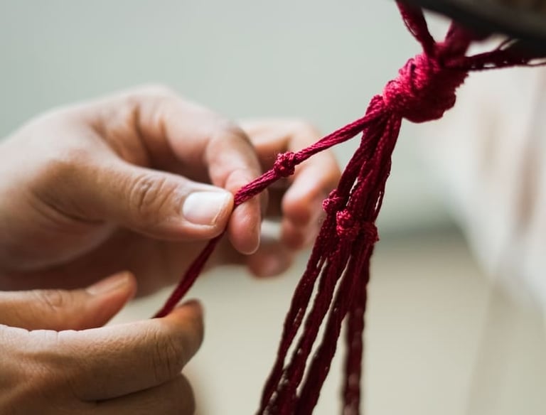 Manos realizando una pieza de macramé colgante en color rojo.