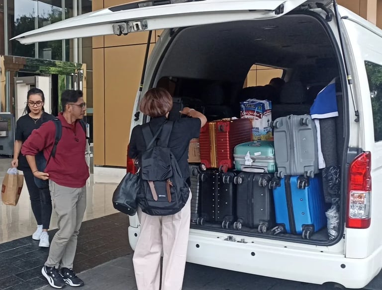 Satu orang pria dua orang wanita sedang menurunkan bagasi dari Hiace.