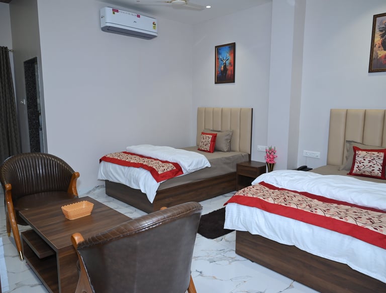 Modern hotel room with twin beds, red decorative runners, and a seating area with leather chairs.