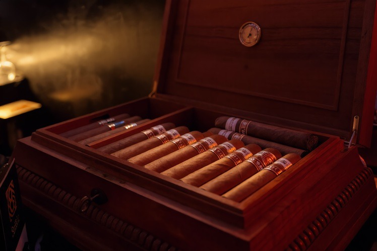 Hand-rolled premium cigars arranged in a wooden humidor box with a built-in hygrometer.