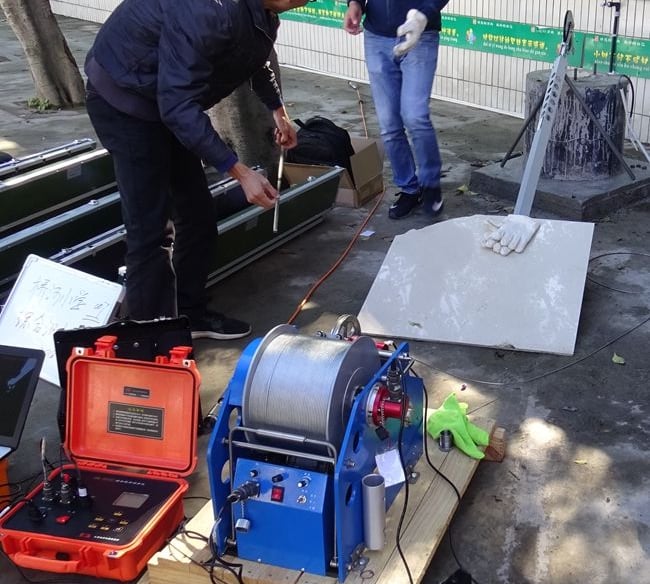 Industrial borewell inspection camera equipment with a motorized cable winch and control unit being operated outdoors.