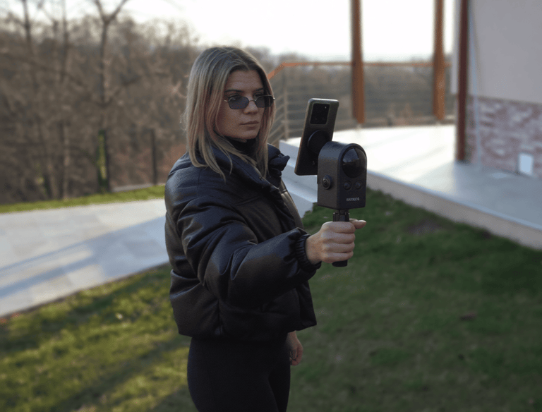 A woman using a handheld 3D scanner and smartphone to capture a digital model outdoors.