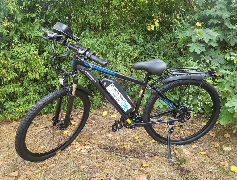 Black electric mountain bike with battery pack parked on a wooded trail.