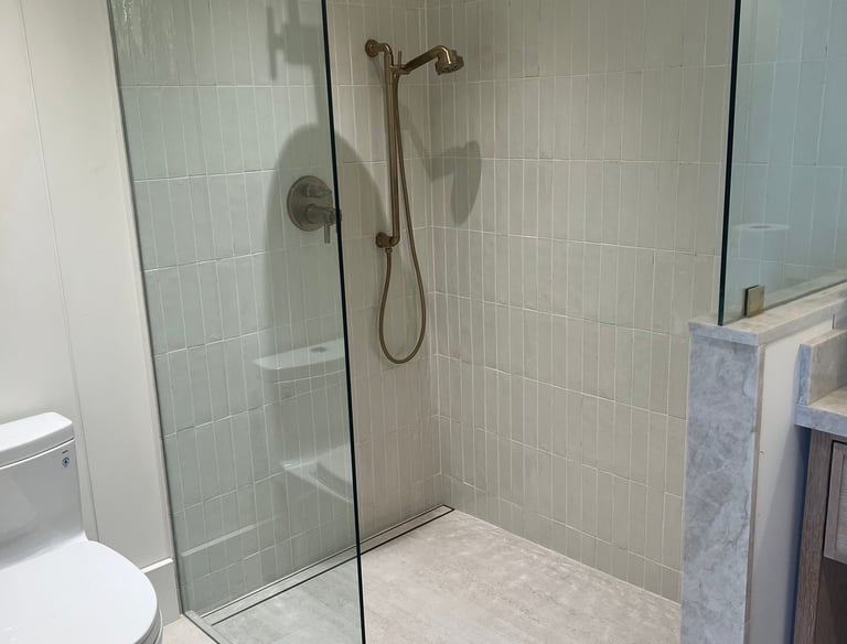 Modern walk-in shower with vertical subway tiles, glass door, and brushed gold rain shower head.