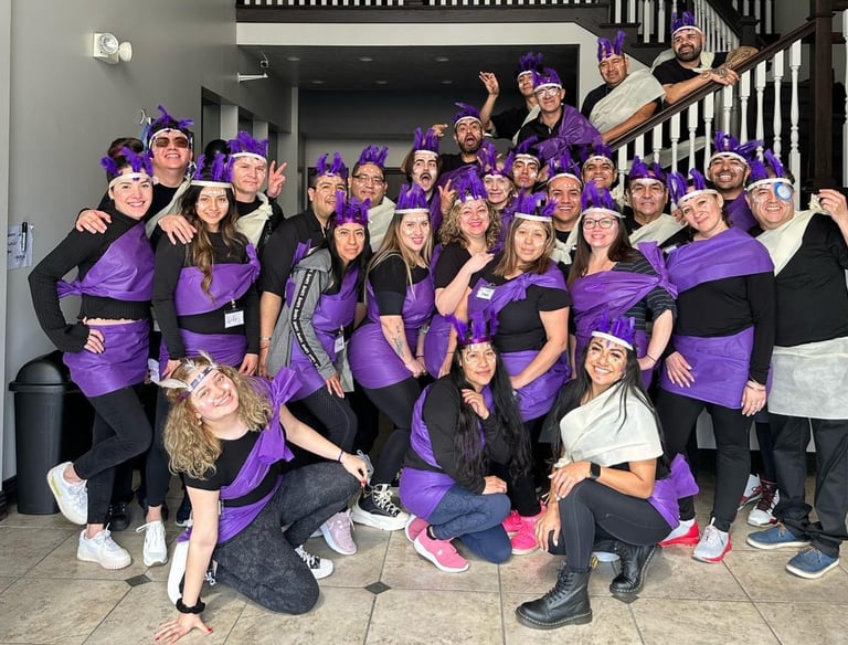 A large group of smiling people posing in matching purple and black team costumes with feather headbands.