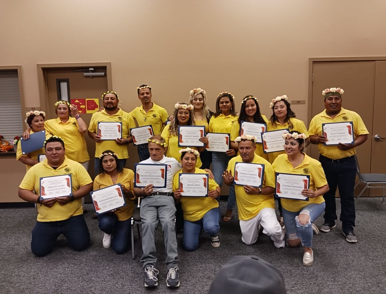 A group of graduates in yellow shirts hold their achievement certificates during a floral crown ceremony.