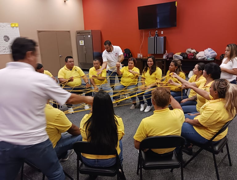 A group of workers in yellow shirts participating in a collaborative team building exercise with yellow ropes.