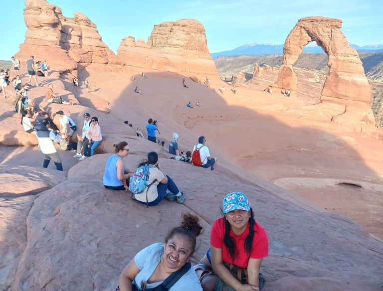 Tourists gathering on red rock formations at Delicate Arch in Arches National Park, Utah.