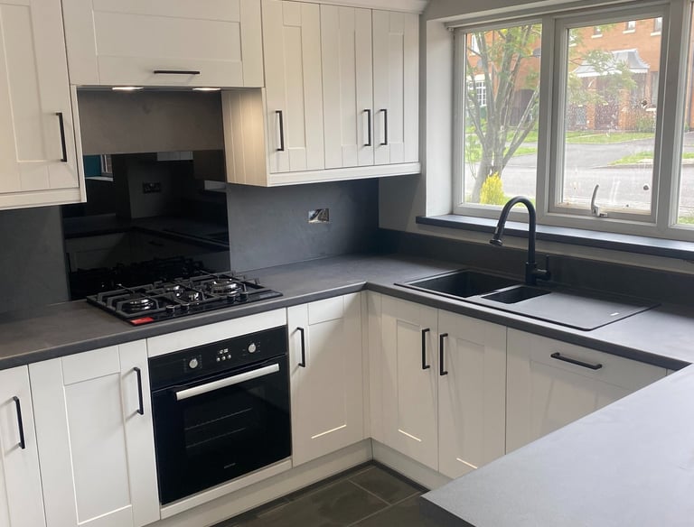 A simple kitchen with white cabinets and grey worktops.