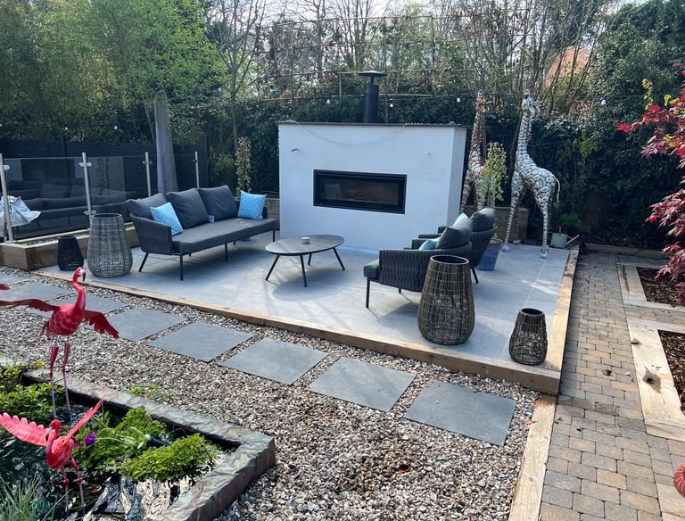 An outdoor living area with grey sofas and a fireplace built into a white rendered wall.