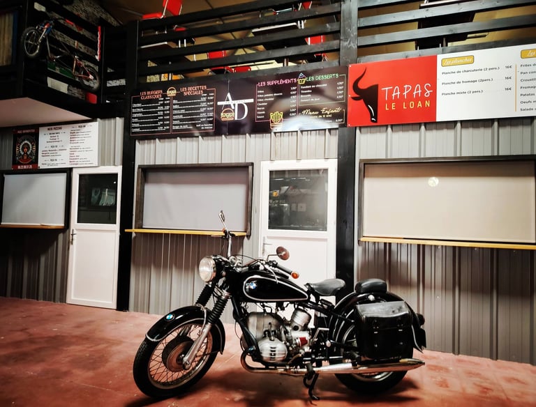 Moto de collection exposée devant le bar de la brasserie vintage dans l'ambiance garage 50s.
