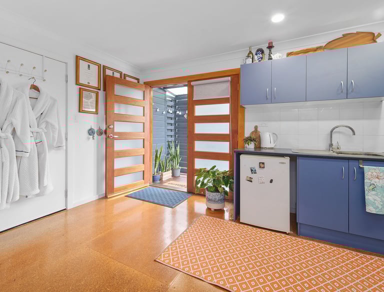 Kitchenette at Marche Home Stay with blue cabinets, a small fridge, bathrobes, and doors opening to a cosy outdoor area.